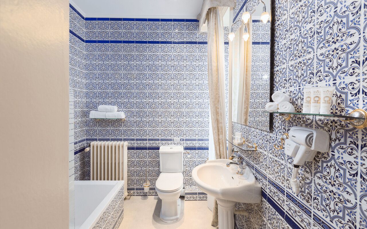 A bathroom with blue and white patterned tiles, a white toilet, a sink, and a towel rack.