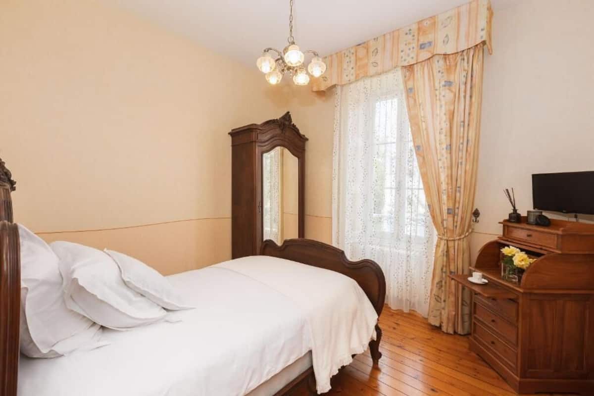 Quarto com cama de madeira, cômoda, espelho e televisão sobre um móvel de madeira.