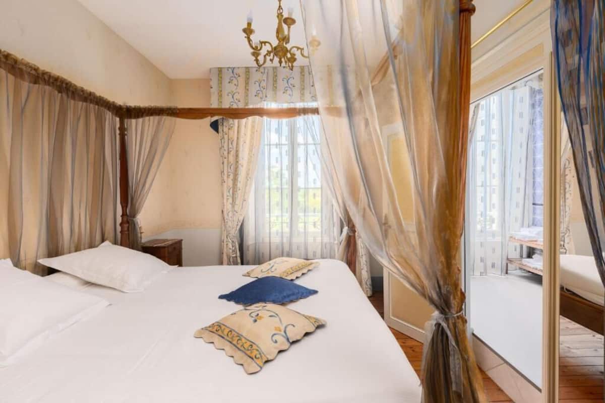 Quarto com uma cama grande, um lustre e cortinas finas.
