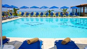 A clear blue pool with lounge chairs and umbrellas, surrounded by palm trees and a view of the ocean. - Krini Beach Hotel (Rethymno)