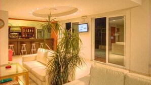 A living room with a sofa, a coffee table, a TV, and a plant. - Krini Beach Hotel (Rethymno)