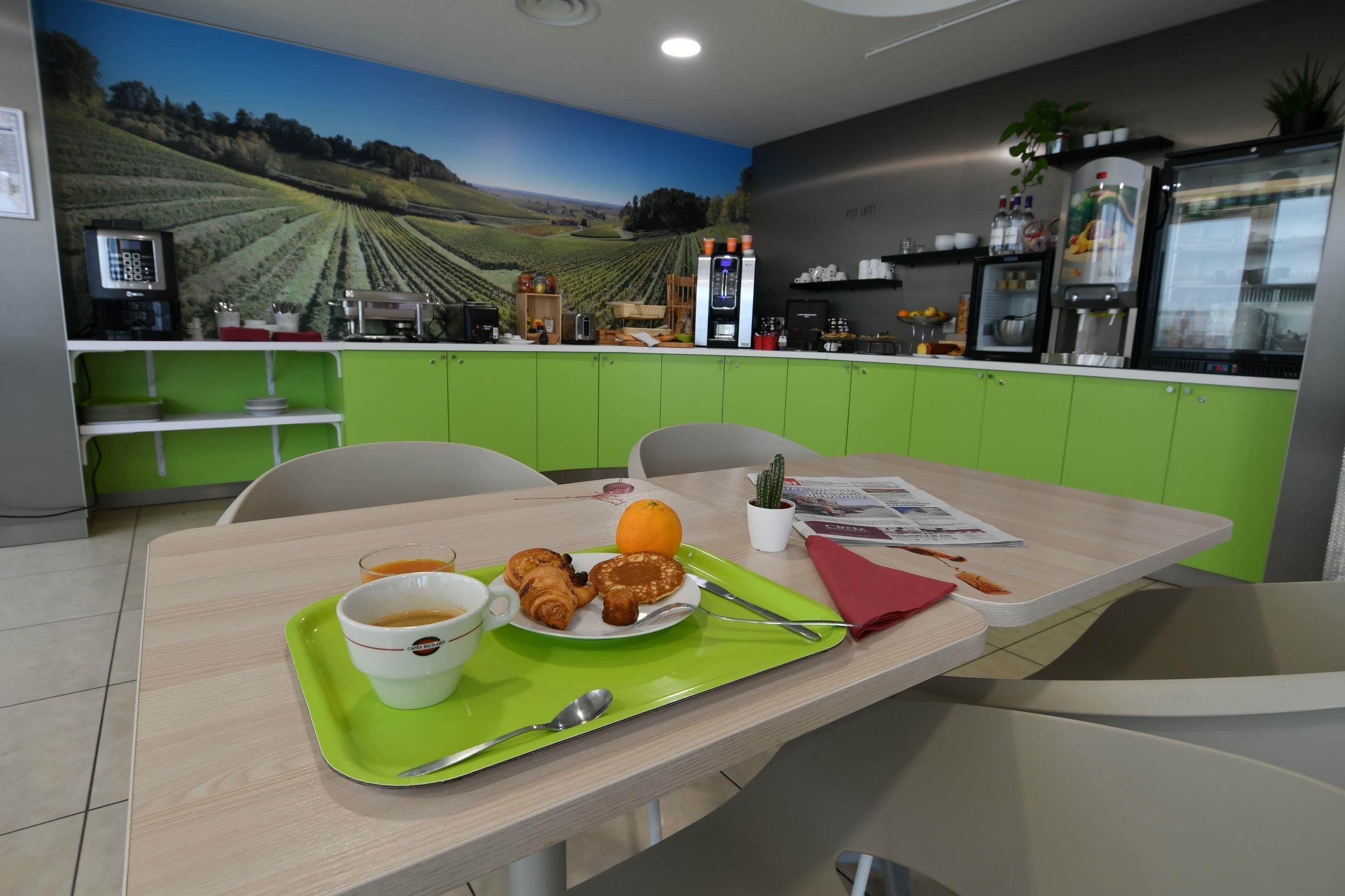 A dining area with a table set for breakfast, including croissants, an orange, and a beverage.