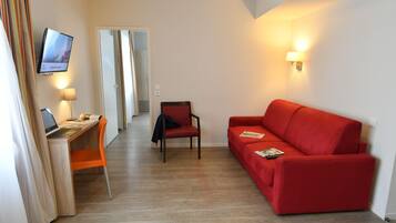 Ein Hotelzimmer mit einem Holztisch, einem roten Sofa, einem an der Wand befestigten Fernseher und einer Lampe.