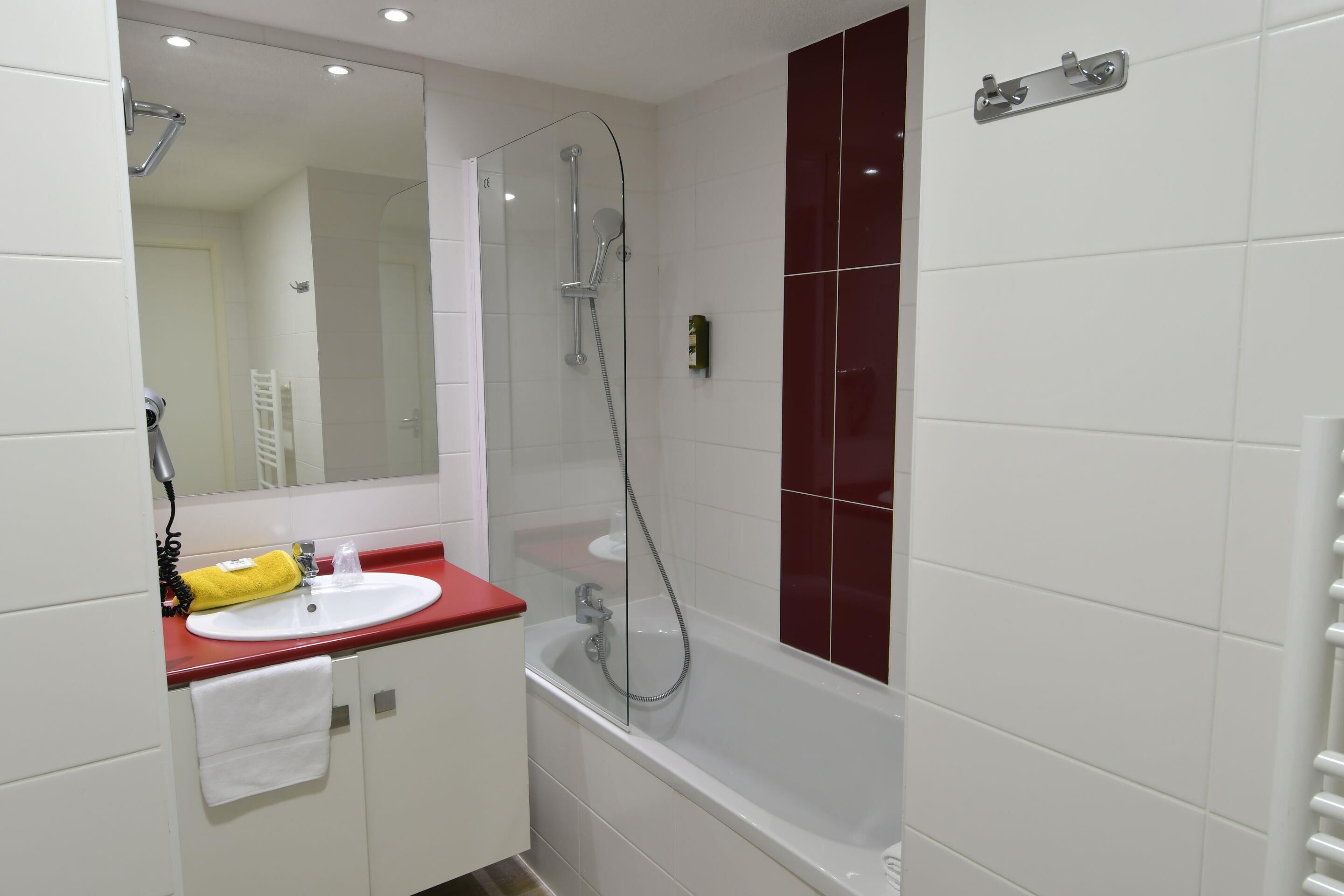 Een badkamer met een wit wastafelmeubel, een rode werkblad en een douche met glazen wanden.