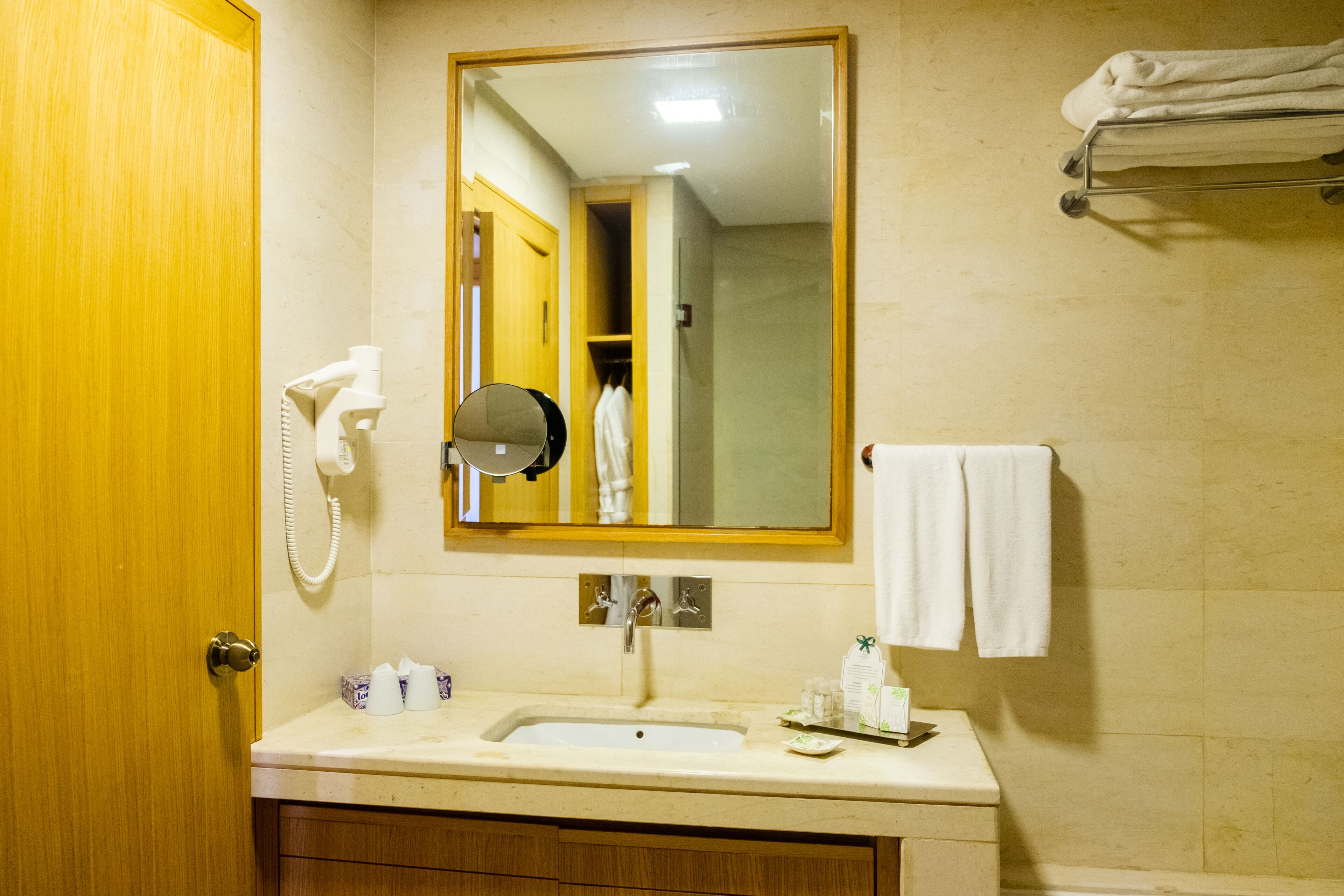 Un baño con lavamanos, espejo, toallero y una puerta de madera.