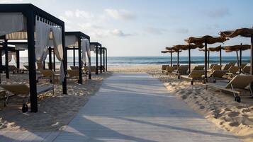 Un paseo marítimo en la playa con tumbonas y zonas de estar cubiertas, que conduce al océano.