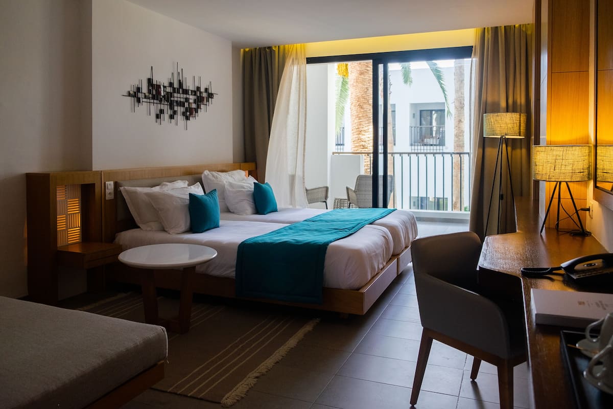 Une chambre d’hôtel avec un lit, un bureau, une chaise, une petite table et un balcon avec vue.
