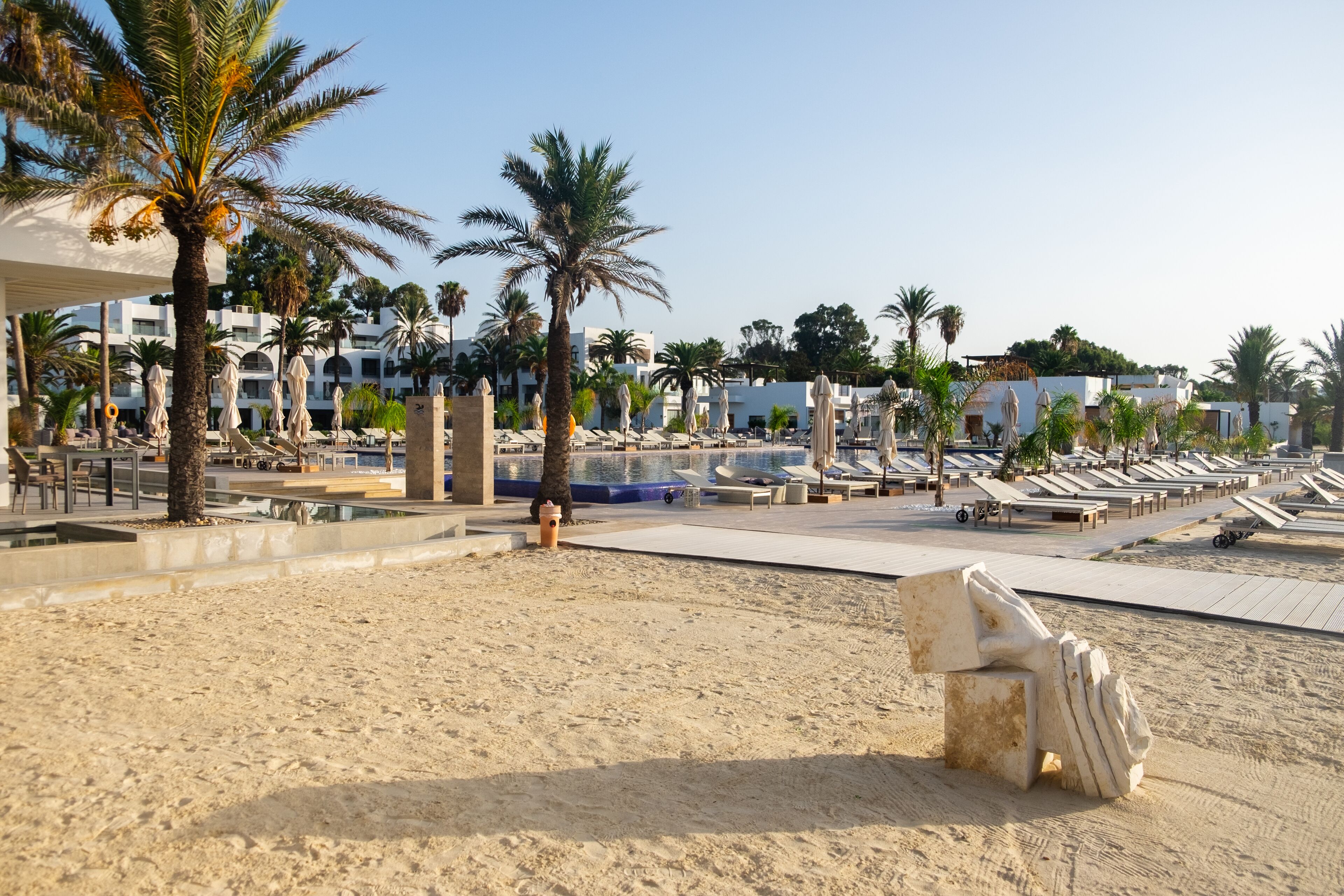 Un resort en la playa con tumbonas, palmeras y una zona de piscina.