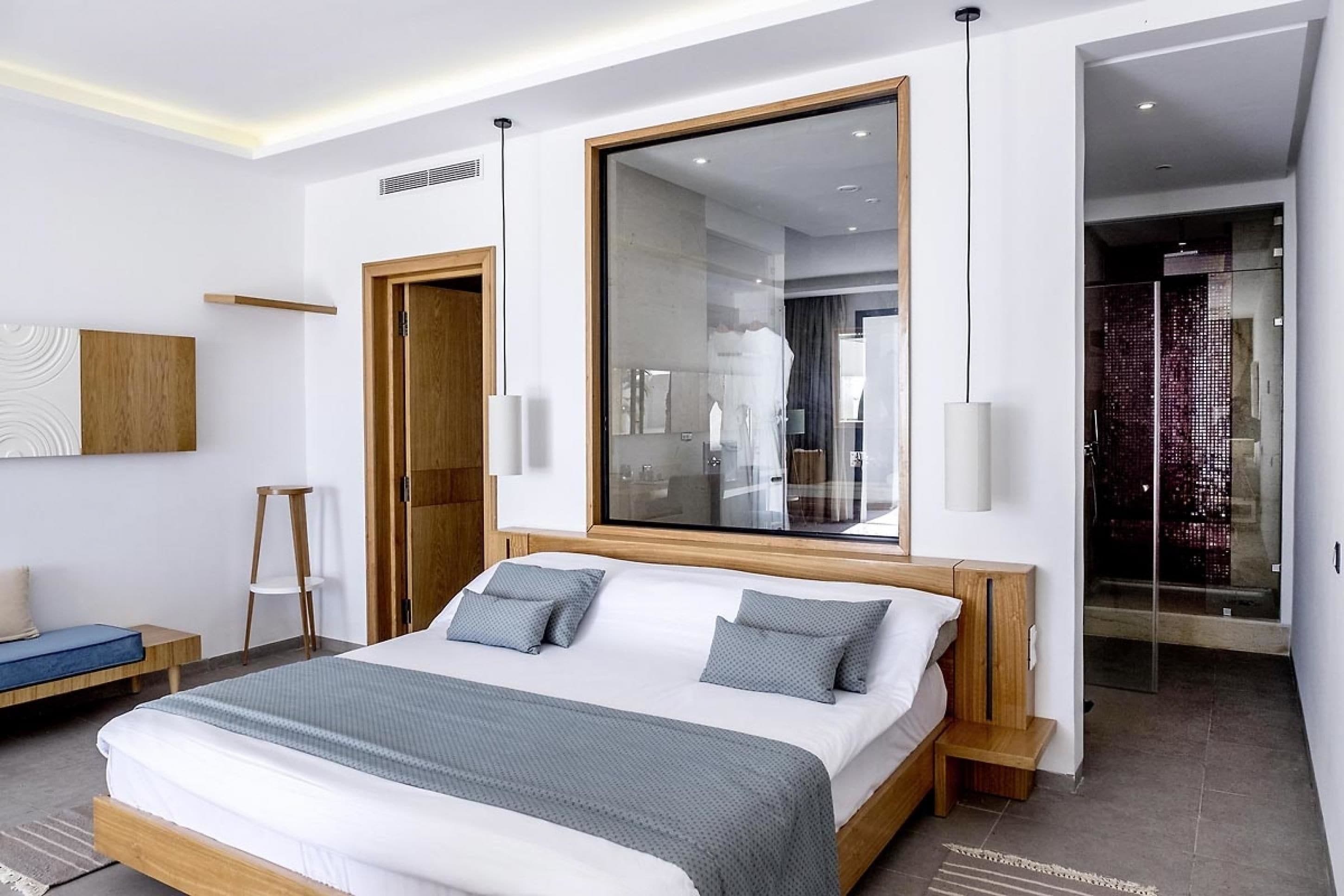 Et moderne hotelværelse med en stor seng, et træhovedgærde, et stort spejl og et brusekabine i glas.