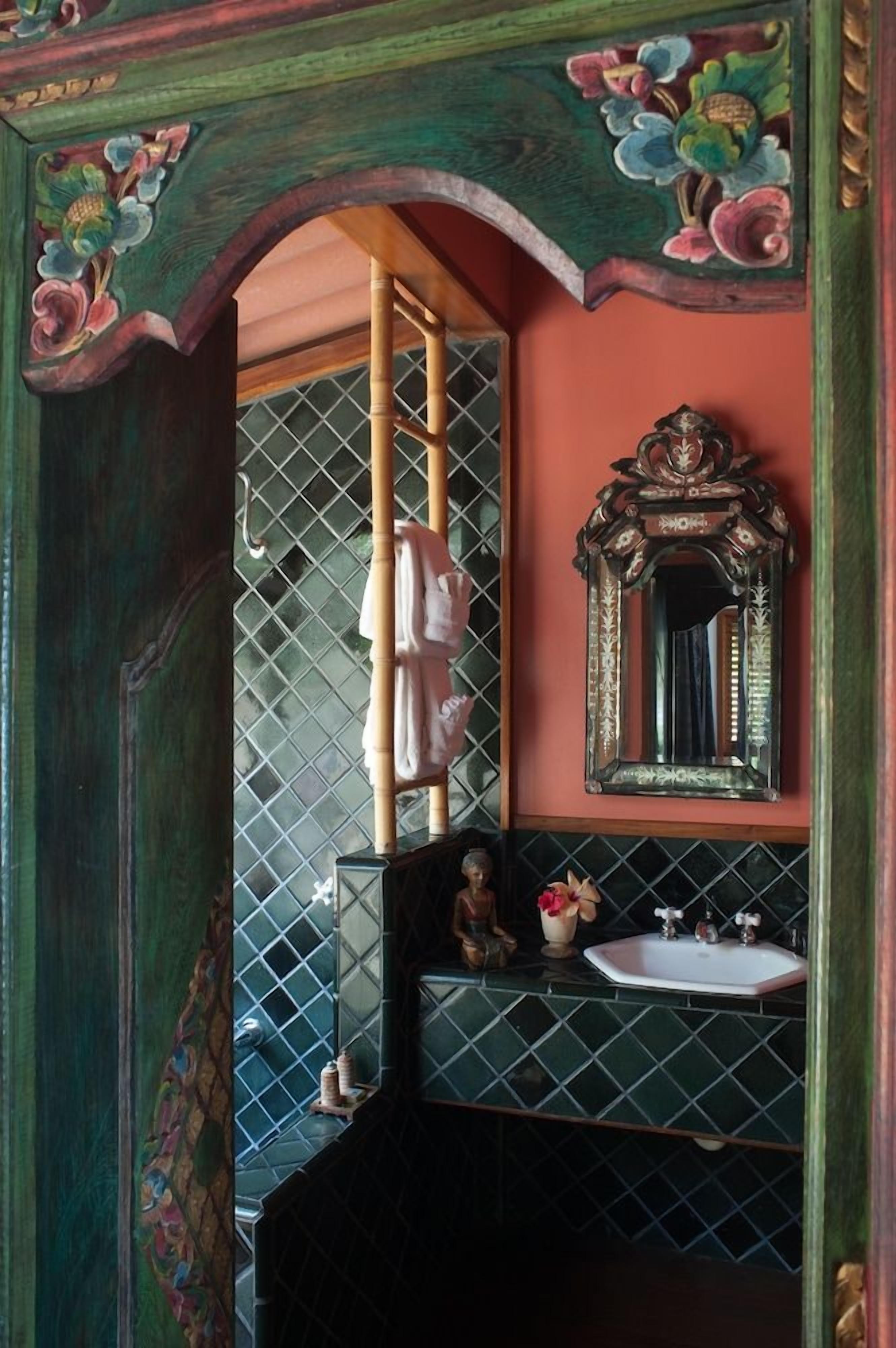 A bathroom with a green door, a mirror, a sink, and a decorative towel rack.