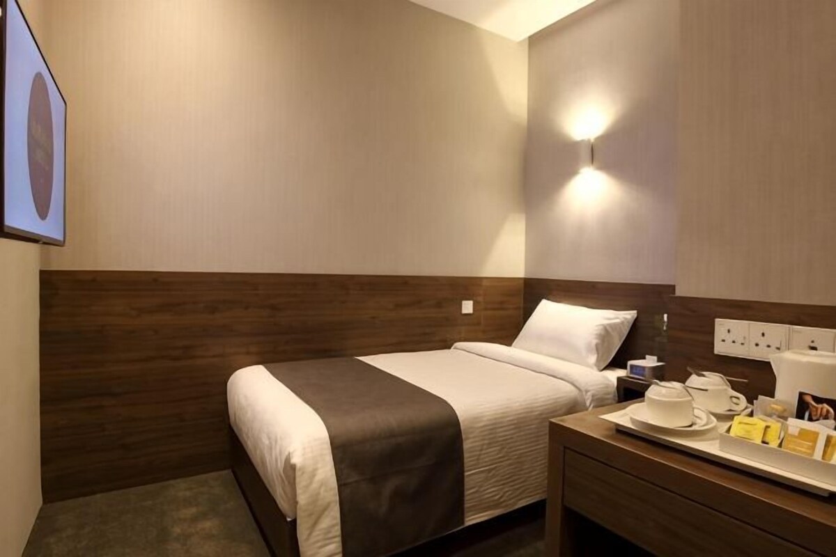 A hotel room with a bed, bedside table, and a wall-mounted light fixture.