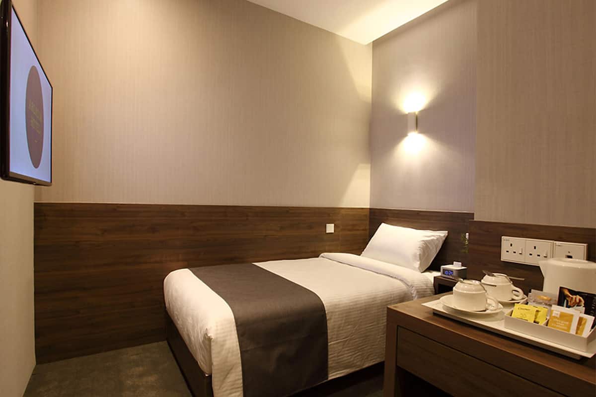 A hotel room with a bed, bedside table, and a wall-mounted light fixture.