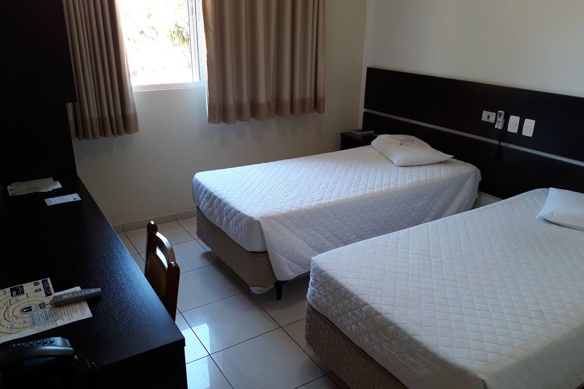 Habitación de hotel con dos camas, un escritorio con teléfono y una ventana con cortinas.