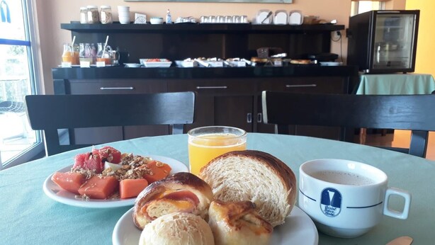 A breakfast setting with a plate of food, a glass of orange juice, and a coffee cup on a table. - Cristal Palace Inn (Lins)