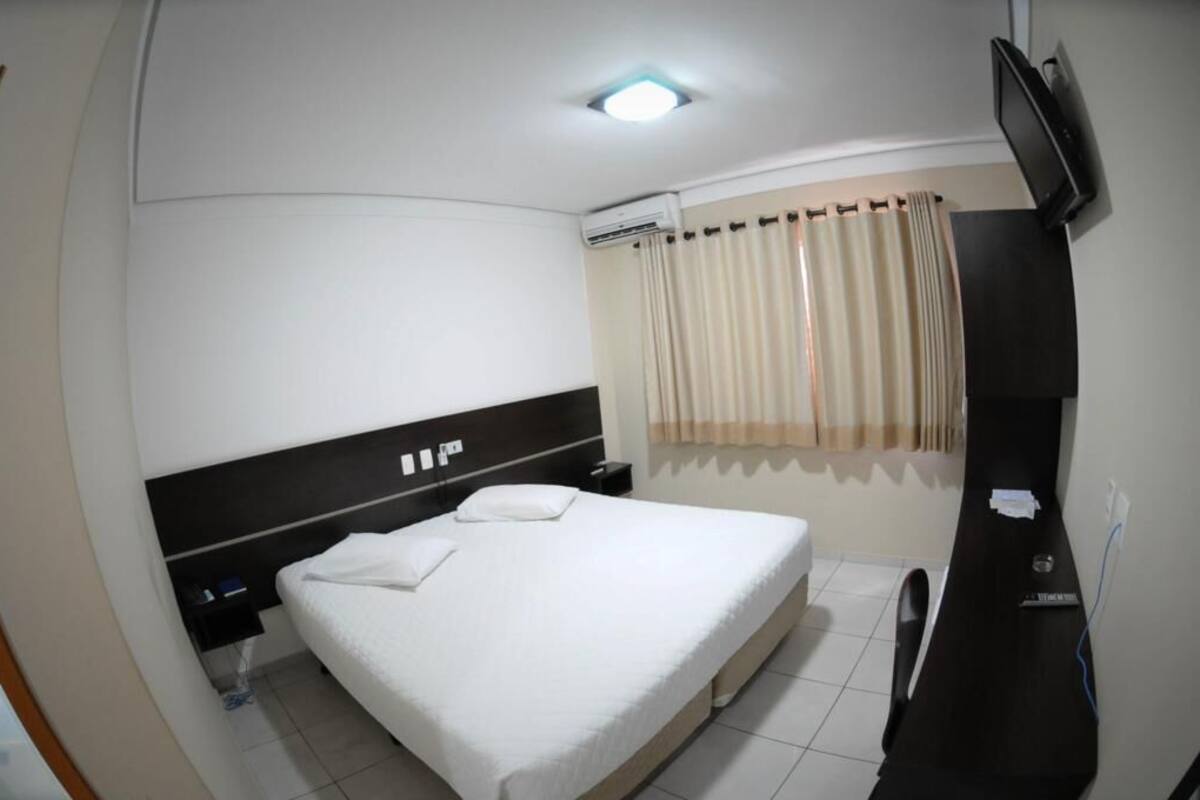 Habitación de hotel con cama, televisor montado en la pared, aire acondicionado y ventana con cortinas.
