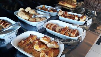 Un bufé con diversas opciones de panadería, incluyendo pão de queijo, pão de queijo con jamón y pão de queijo con queso.