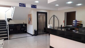 A hotel reception area with a staircase, a reception desk, a painting, and directional signs. - Cristal Palace Inn (Lins)