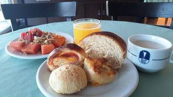 A breakfast plate with toast, muffins, and a fruit salad, a glass of orange juice, and a cup of coffee on a table.