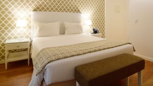 A hotel room with a large bed, two bedside lamps, a bedside phone, and a bench.