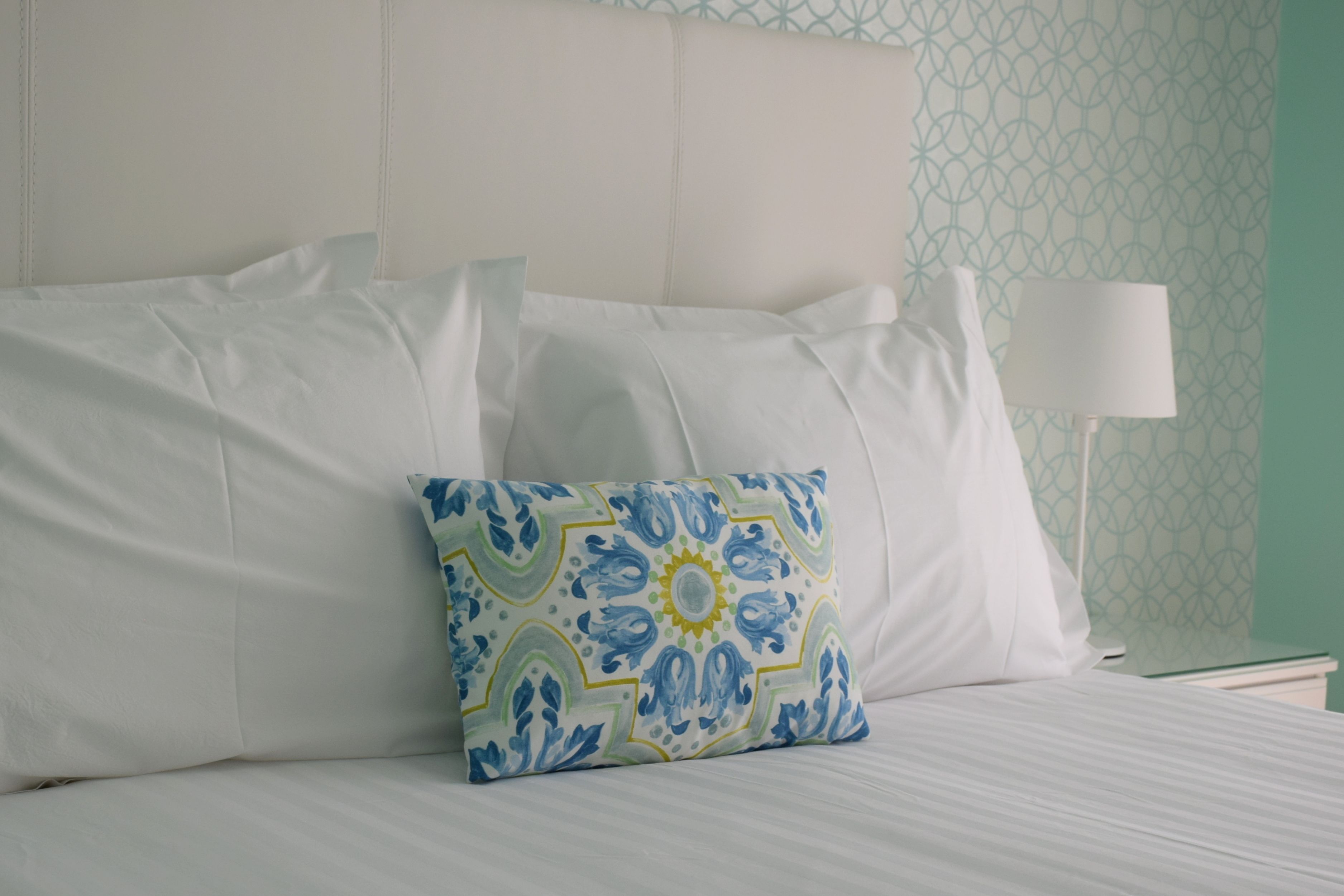 A neatly made bed with white linens and a decorative pillow with a geometric pattern.