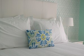 Un lit bien fait, avec du linge de lit blanc et un coussin décoratif orné d’un motif géométrique.