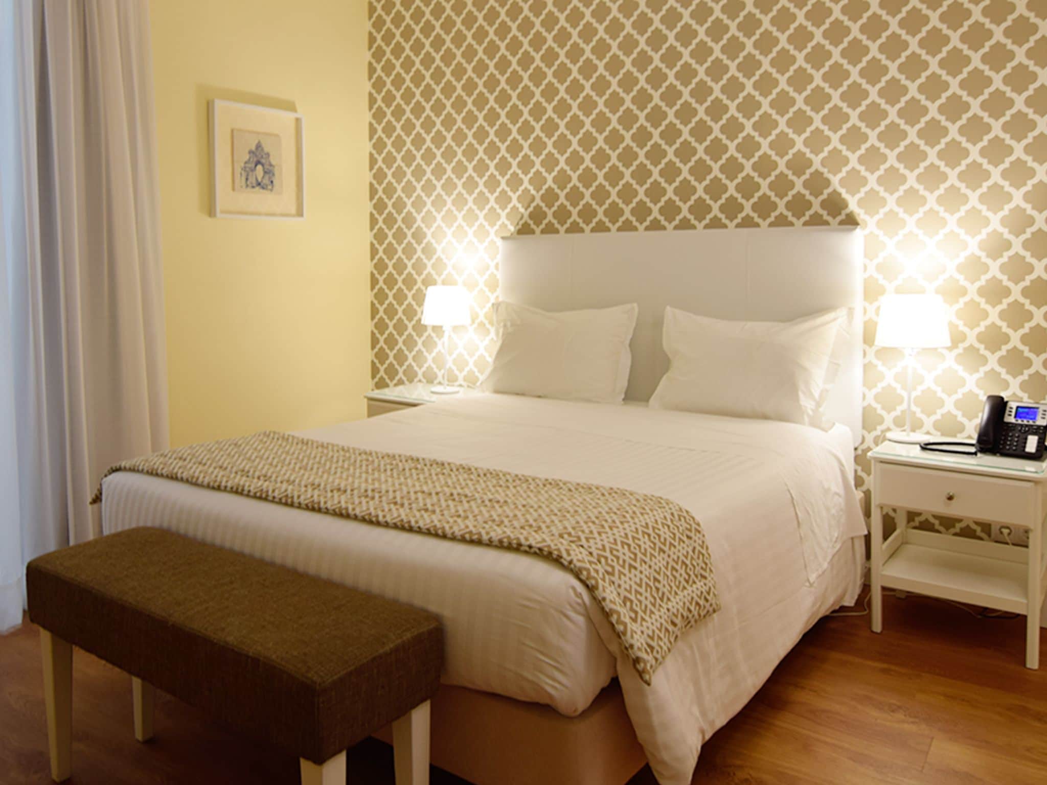 Una cama bien hecha con una colcha estampada, una mesita de noche con una lámpara y un teléfono.