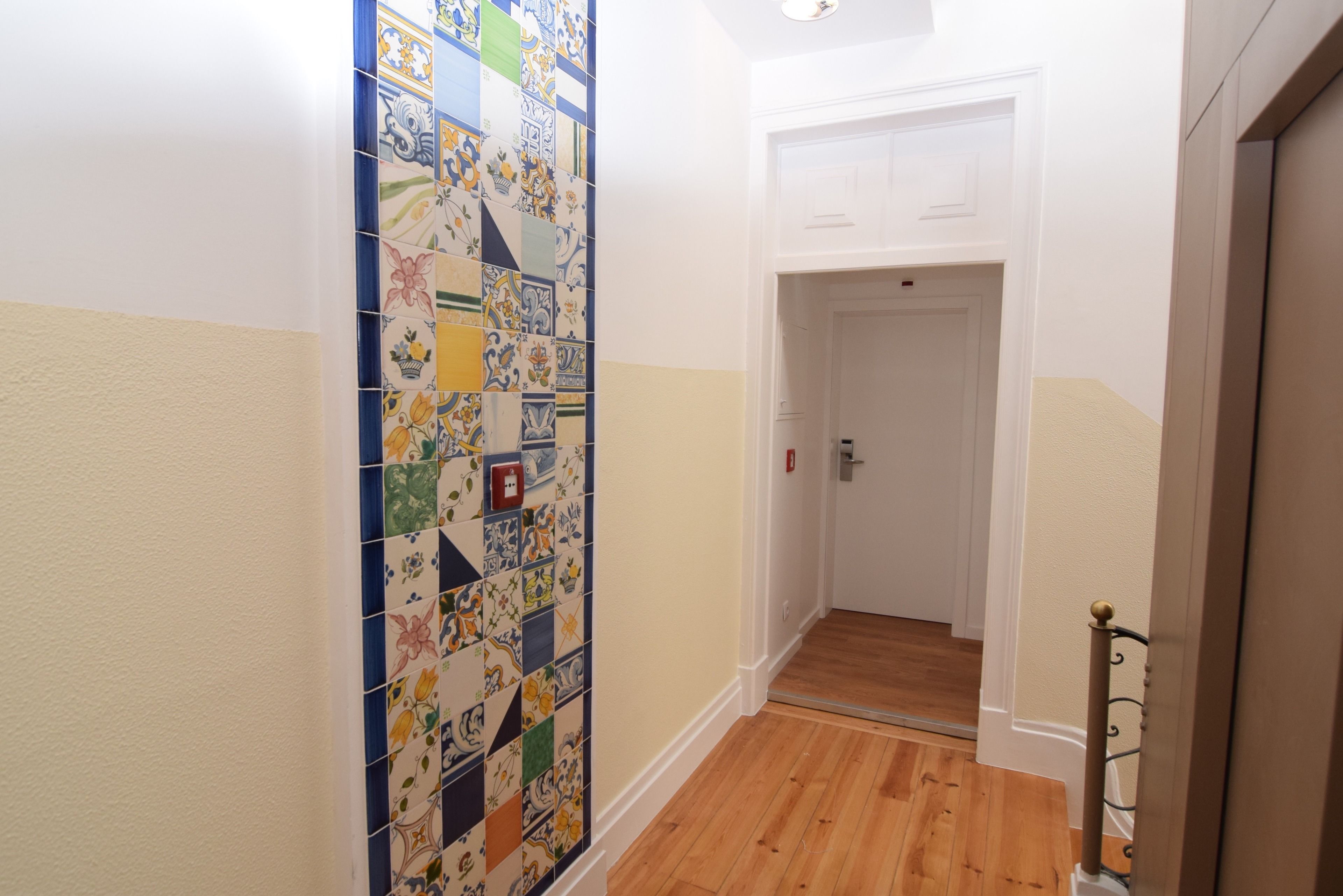 A hallway with a tiled wall, wooden flooring, and a white door at the end.