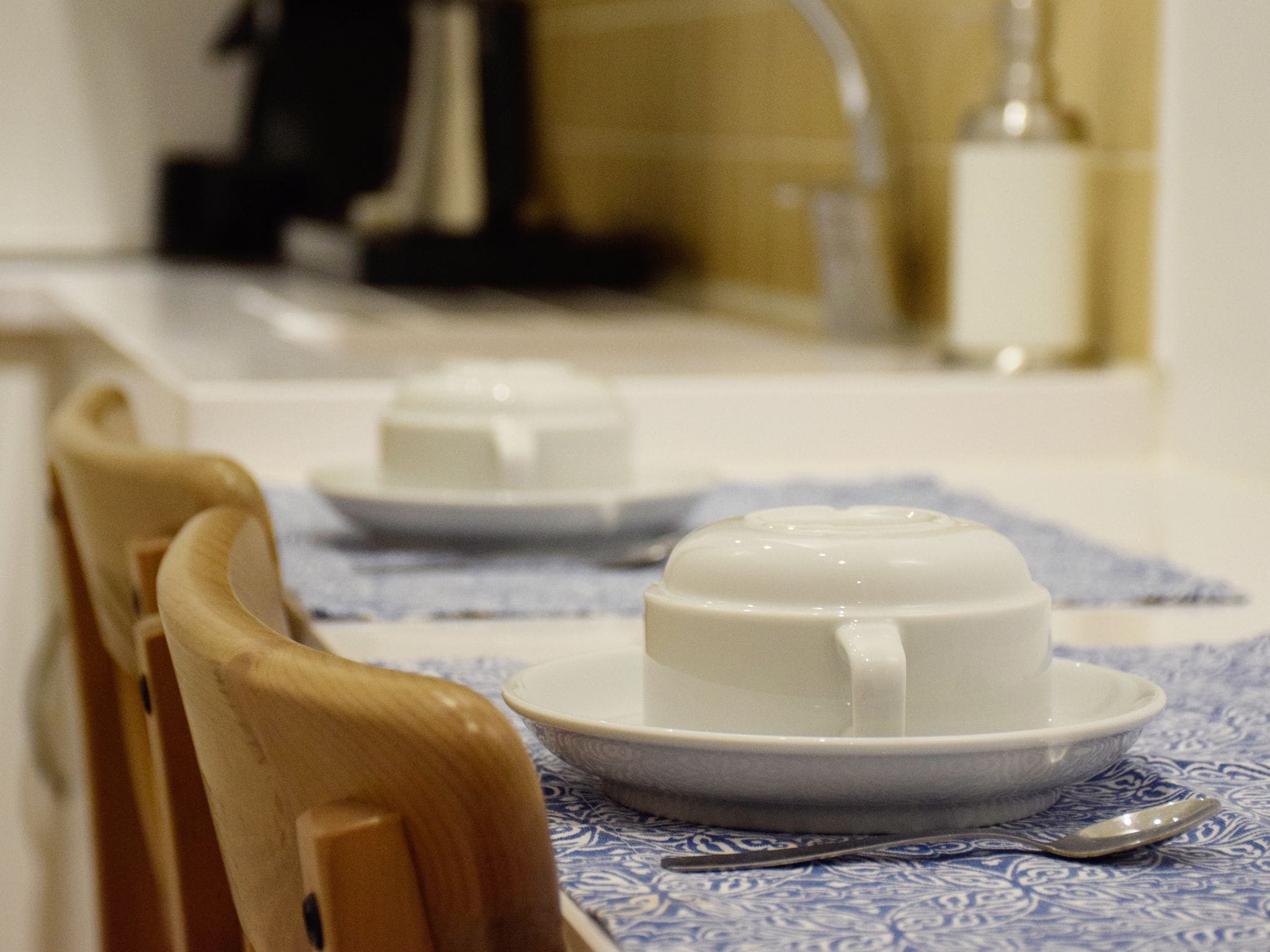 Une table à manger avec une théière blanche, une tasse et une soucoupe, le tout posé sur une nappe bleue à motifs.
