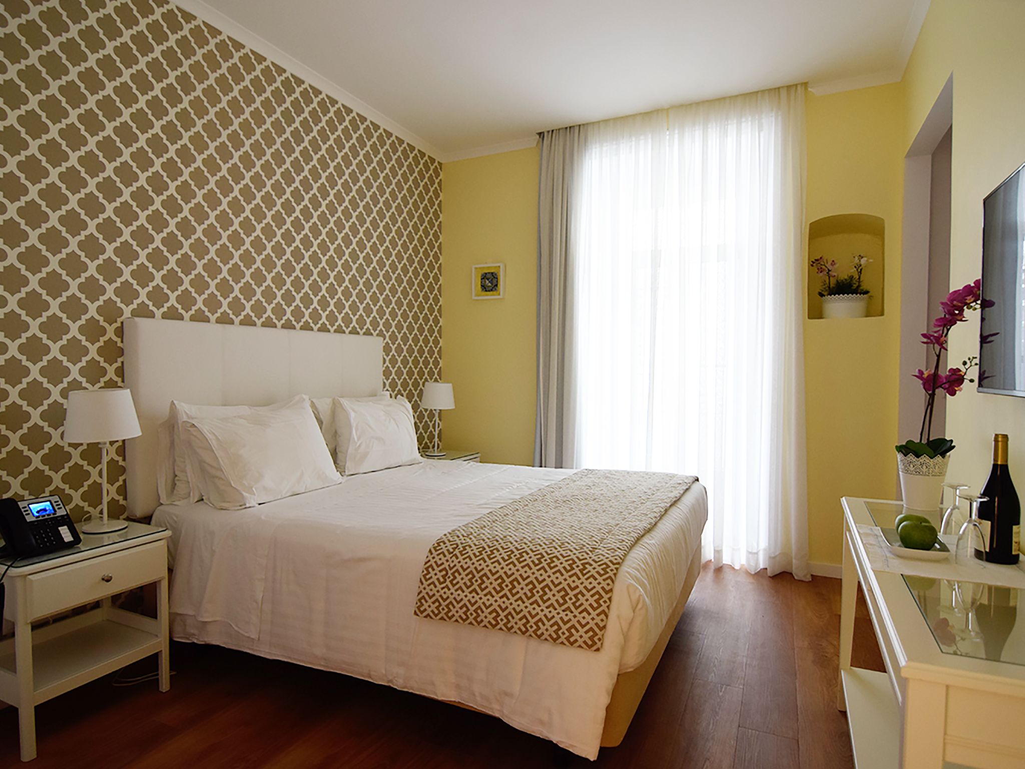Una habitación de hotel con una cama grande, mesitas de noche, un espejo y una pequeña planta en maceta.