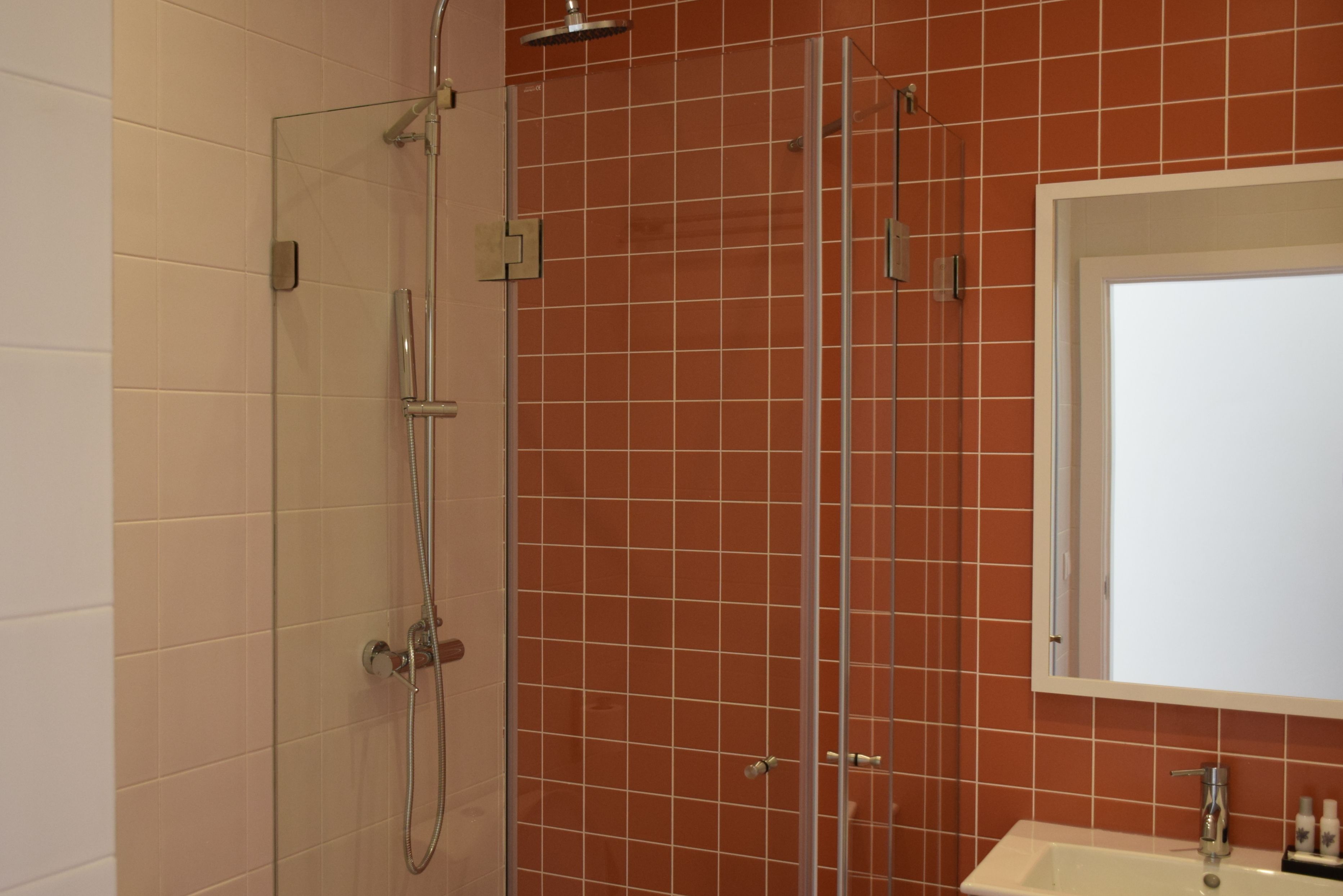 A bathroom with a glass-enclosed shower, a sink, and a mirror above it.