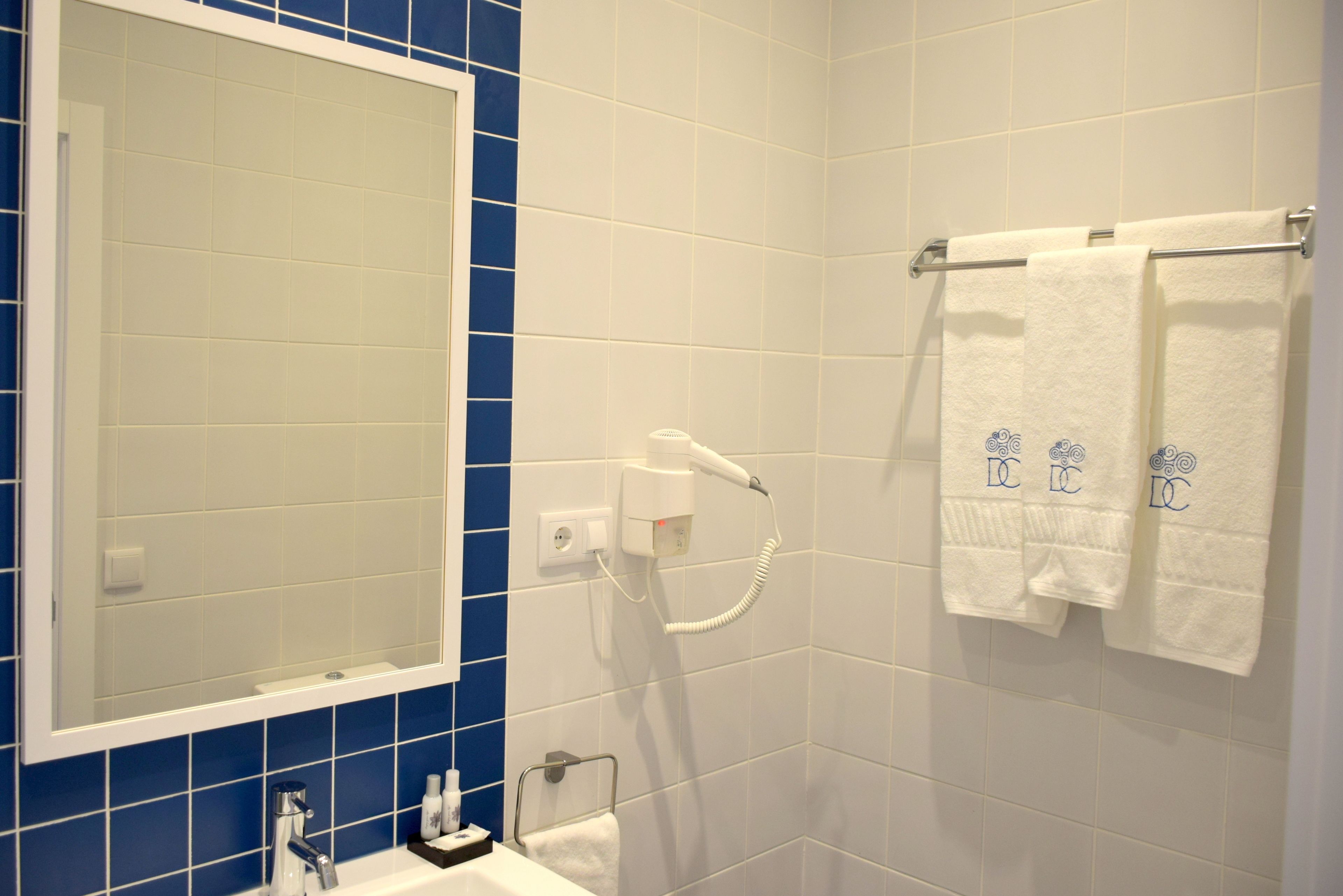 A bathroom with a large mirror, a hairdryer, and two towels with a logo.
