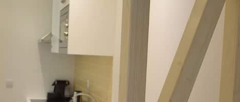 A kitchen with white cabinets, a wooden chair, and a countertop with a coffee machine.