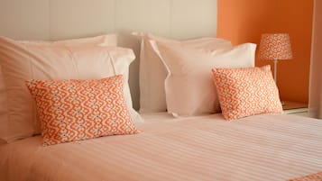 Una cama con almohadas de diseño blanco y naranja, un cabecero blanco y una lámpara sobre una mesita de noche.