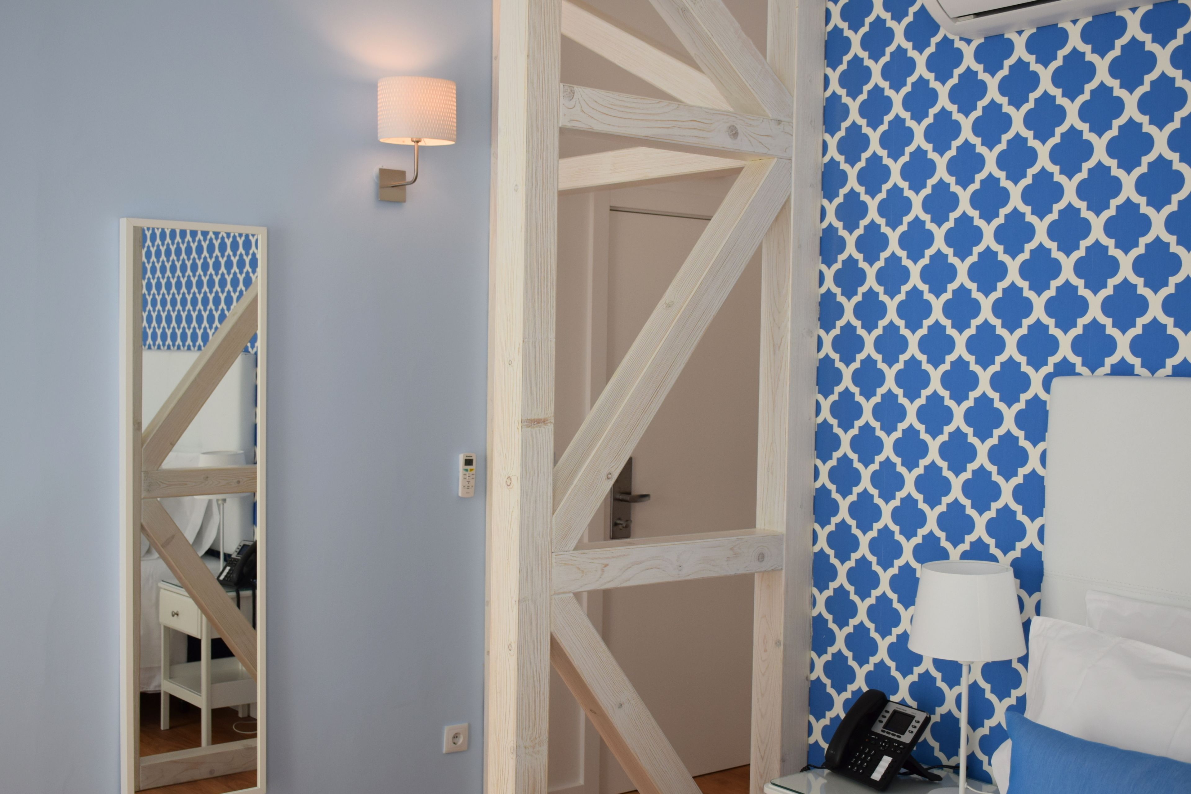 Habitación de hotel con escalera de madera, pared con diseño, mesita de noche con lámpara y teléfono.
