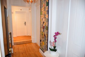 Een gang met een houten vloer, een witte deur en een wand betegeld met kleurrijke tegels.