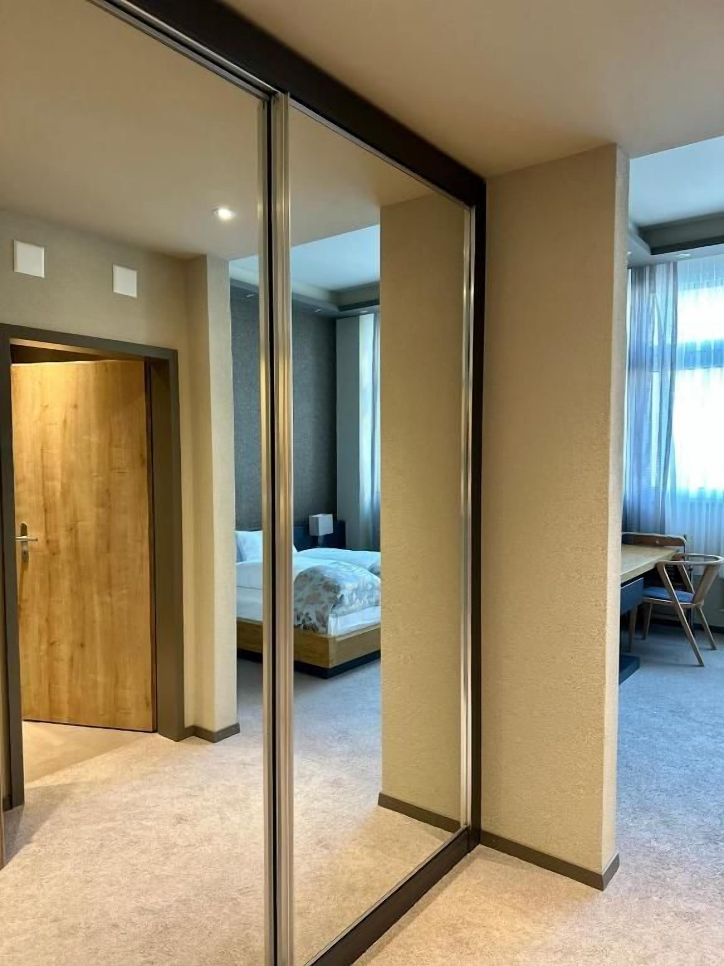 Ein Hotelzimmer mit großem Spiegel, einem Bett, einem Schreibtisch und Blick auf das angrenzende Zimmer.