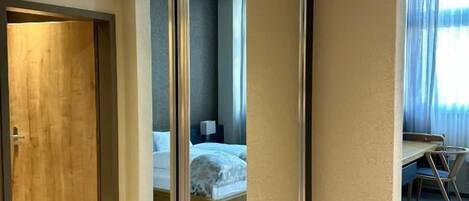 Habitación de hotel con un espejo grande, una cama, un escritorio y vista de la habitación contigua.