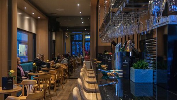 A restaurant with a bar area, seating arrangements, and a view of the street outside. - Plaza Hotel (Winterthur)