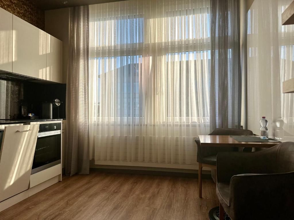 Une cuisine moderne avec un coin repas, comprenant une grande fenêtre avec des rideaux légers, un four encastré et une table à manger avec des chaises.