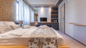A modern hotel room with a large bed, a flat-screen TV, a seating area with a table, and a fireplace. - Plaza Hotel (Winterthur)
