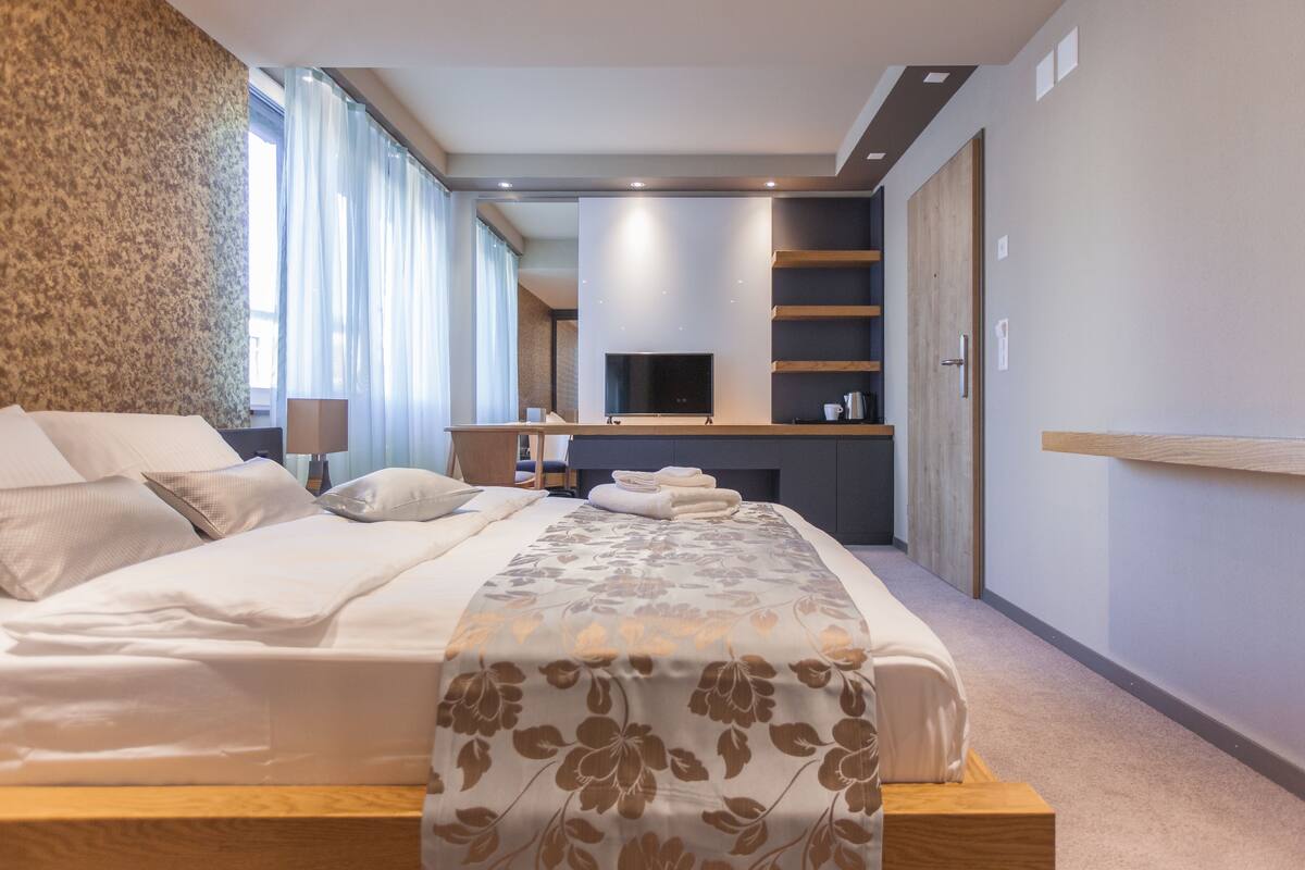 A modern hotel room with a large bed, a flat-screen TV, a seating area with a table, and a fireplace.