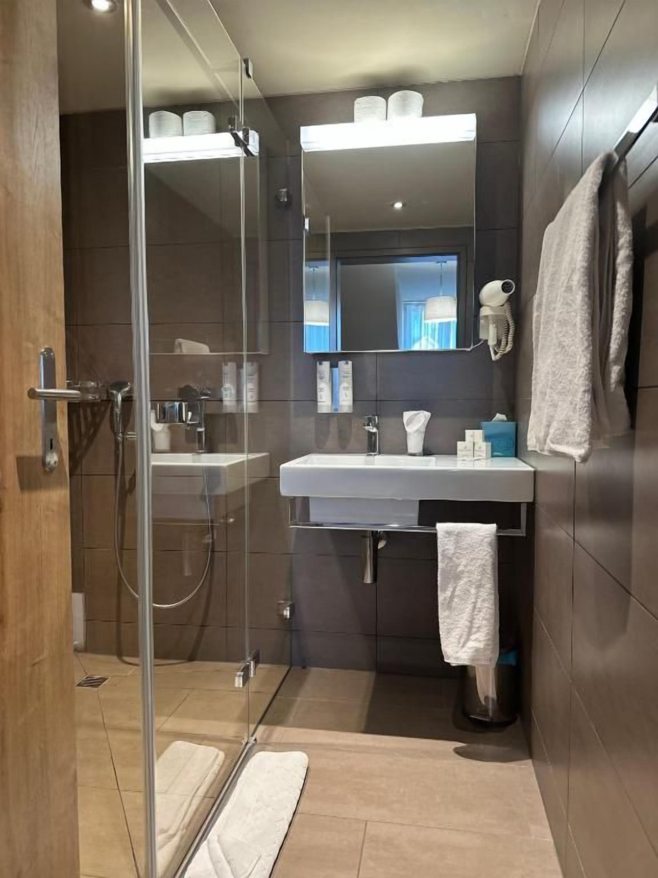 A modern bathroom with a glass shower enclosure, a white sink, and a mirror above the sink.