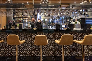 Zona de bar con un cantinero, barra y tres taburetes.