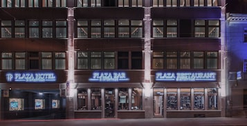 Un edificio de varios pisos con los rótulos 'Plaza Hotel' y 'Plaza Bar', que presenta grandes ventanales y una fachada moderna.