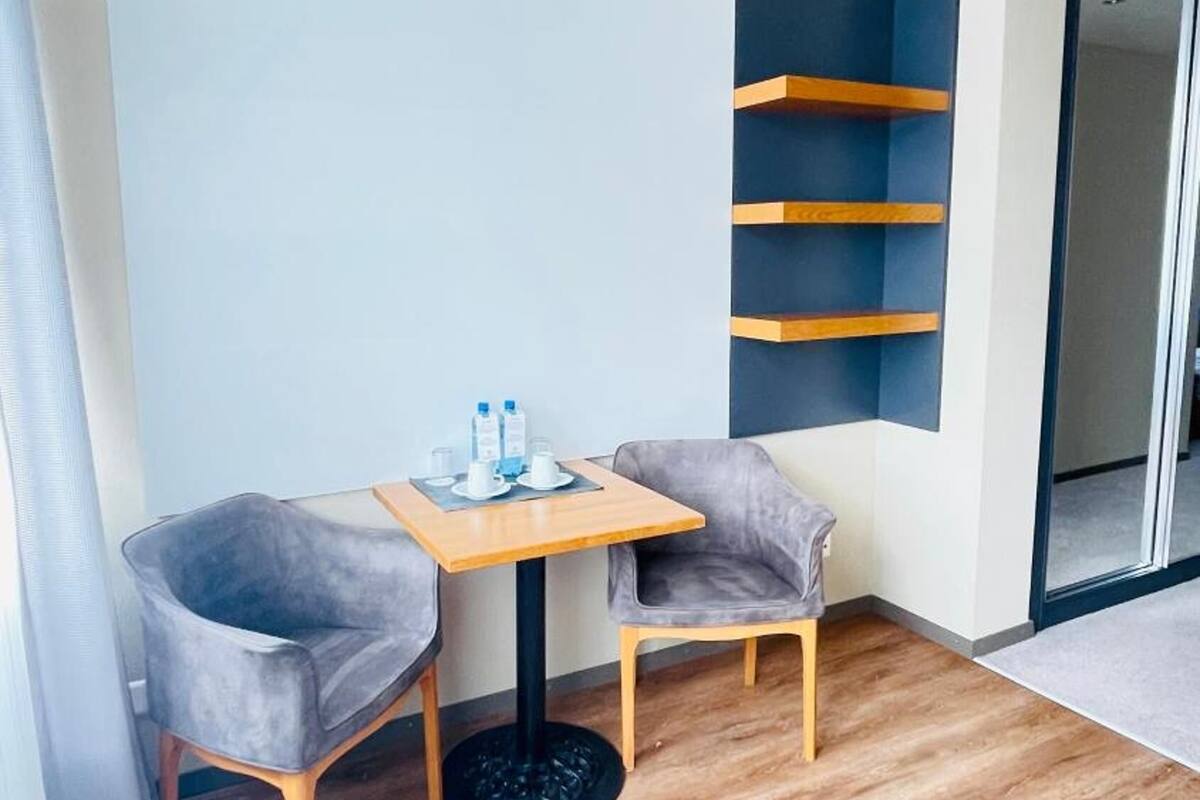 A small, modern room with a wooden floor, two grey chairs, a small table with water bottles, and a blue wall with shelves.