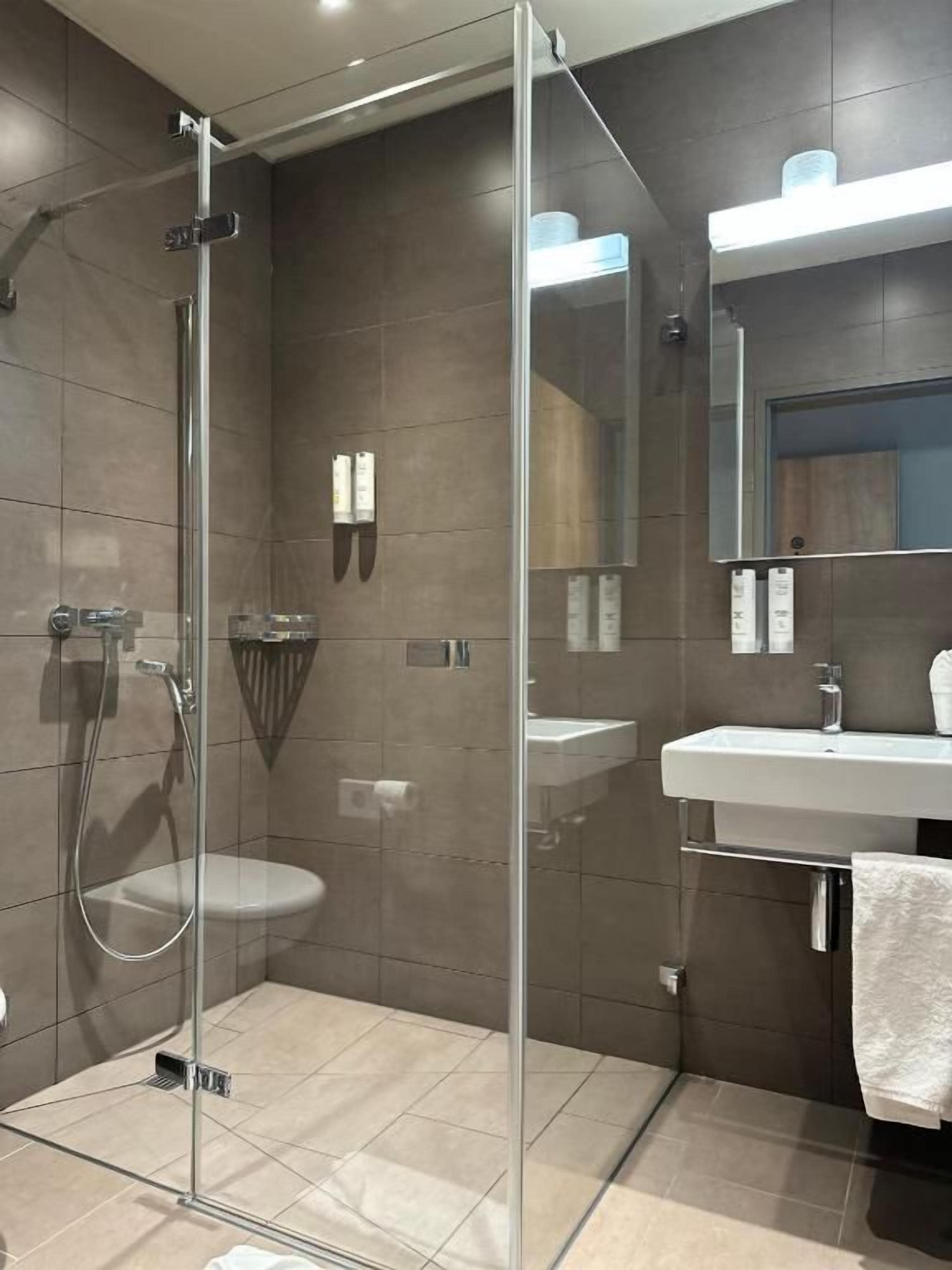 A modern bathroom with a glass-enclosed shower, a white sink, and a mirror above the sink.