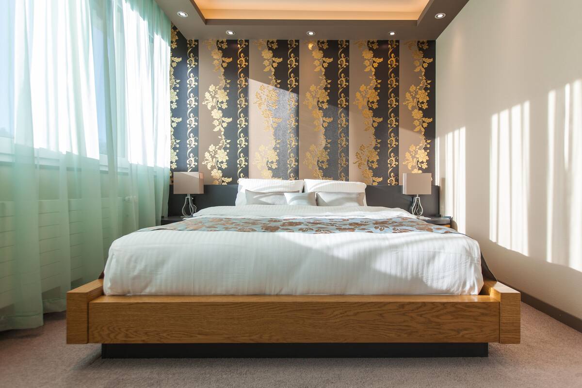 A modern bedroom with a large bed, wooden headboard, and a decorative wall with vertical patterns.