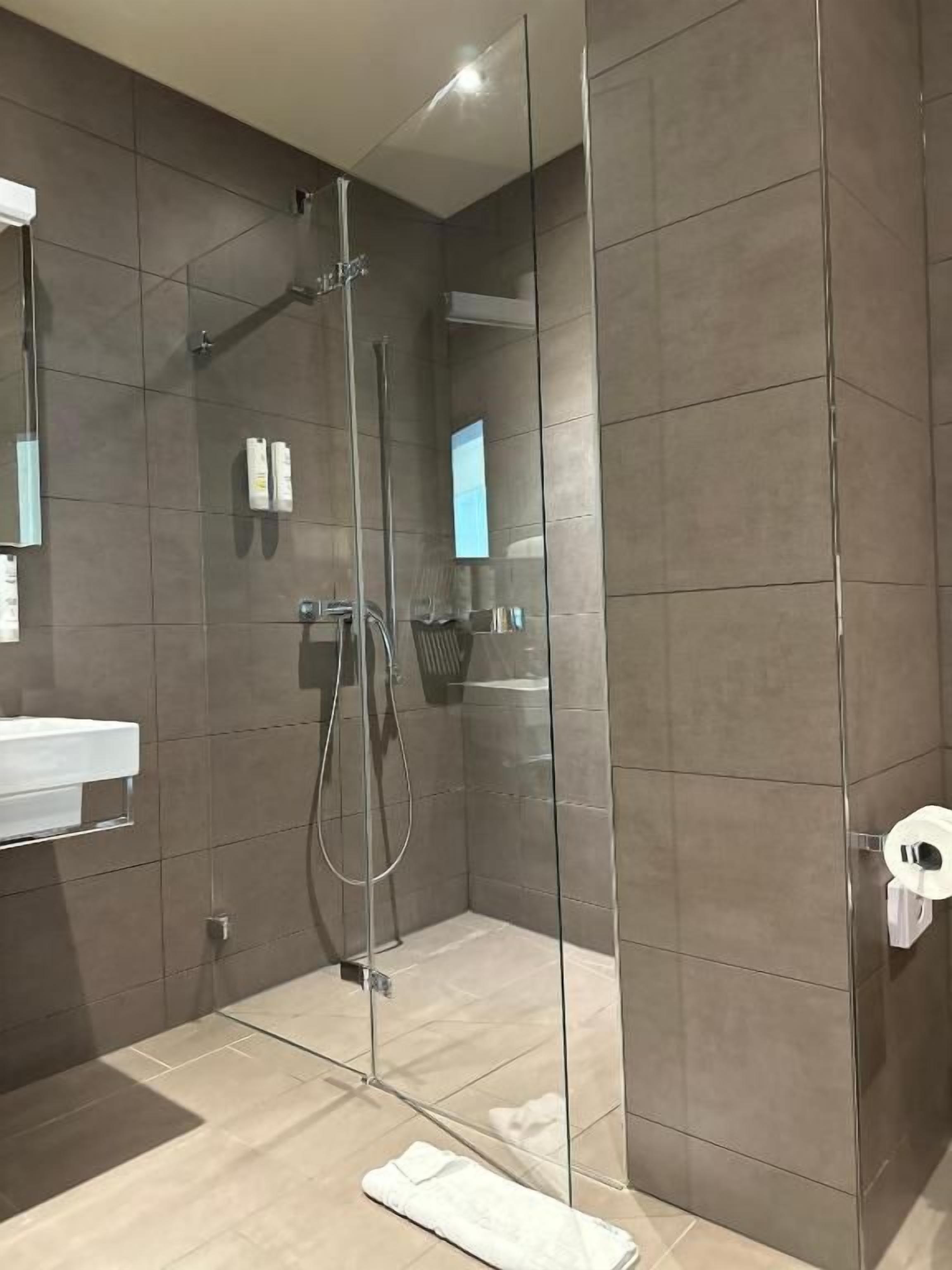 Un baño moderno con ducha de vidrio, lavamanos blanco y perchero para toallas.