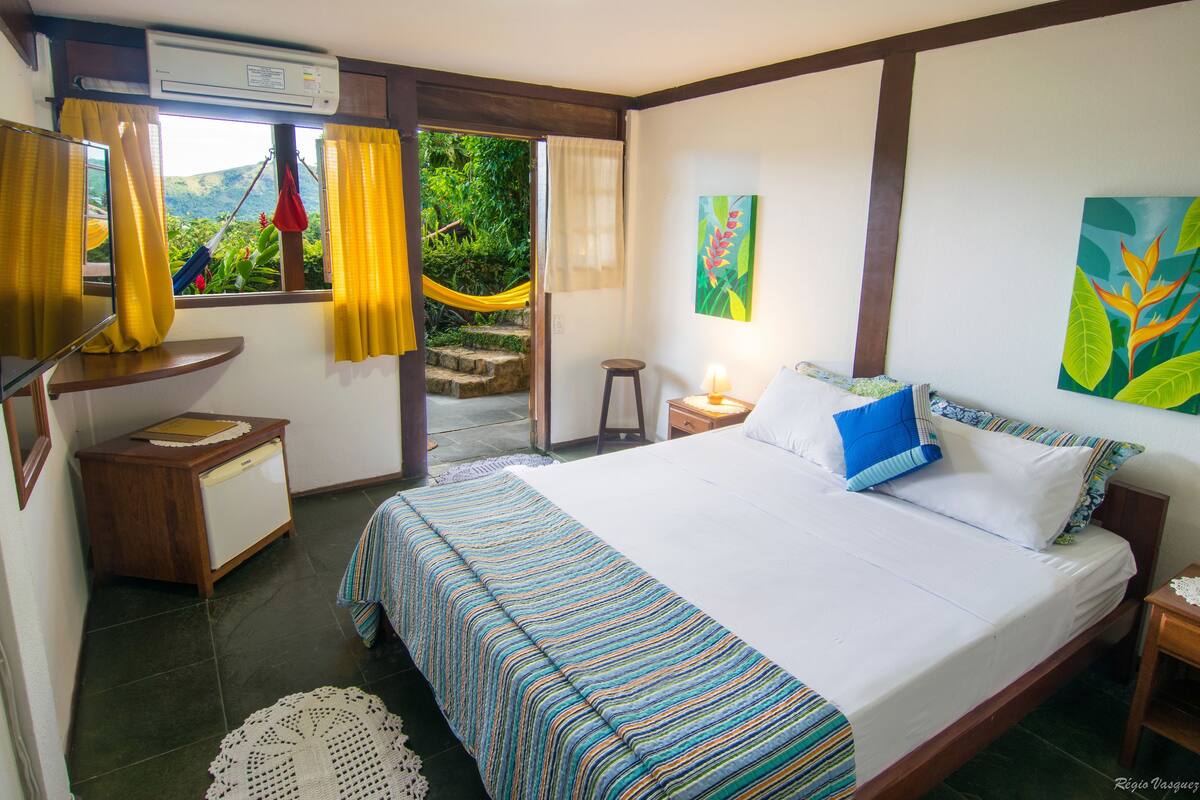 Un dormitorio con cama, mesita de noche, escritorio y ventana con cortinas.