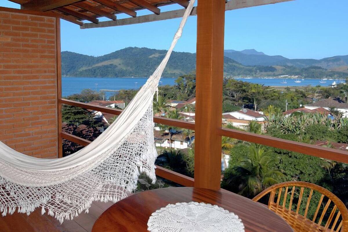 Una hamaca en un balcón con vistas a la costa, casas y colinas.